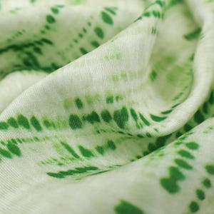 Op de afbeelding: Een zachte, lichtgewicht stof met een witte basis en een levendig groen tie-dye patroon. Het ontwerp bestaat uit horizontale, onderbroken lijnen en verspreide stippen van verschillende groottes, wat zorgt voor een textuurrijk, golvend effect.