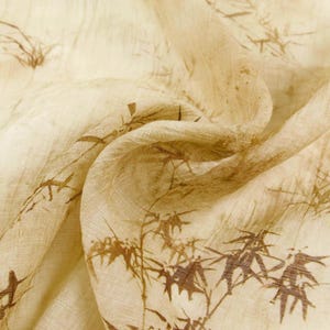May include: Cream-colored fabric with a brown bamboo pattern. The fabric is draped, showing folds and texture. The bamboo design is detailed, with individual stalks and leaves visible. The overall aesthetic is natural and organic.