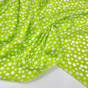 May include: A vibrant lime green fabric featuring a repeating pattern of solid white polka dots of varying sizes. The material is draped in soft folds, creating a textured appearance that highlights the contrast between the bright green and white.