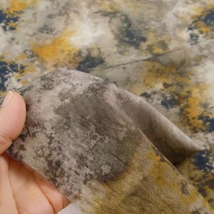 Peut inclure: Un morceau de tissu pr&eacute;sentant un motif abstrait et tachet&eacute; dans des tons de gris fonc&eacute;, charbon et jaune moutarde sourd. Le textile a un aspect textur&eacute; et l&eacute;g&egrave;rement vieilli avec des transitions de couleurs fondues sur la surface.
