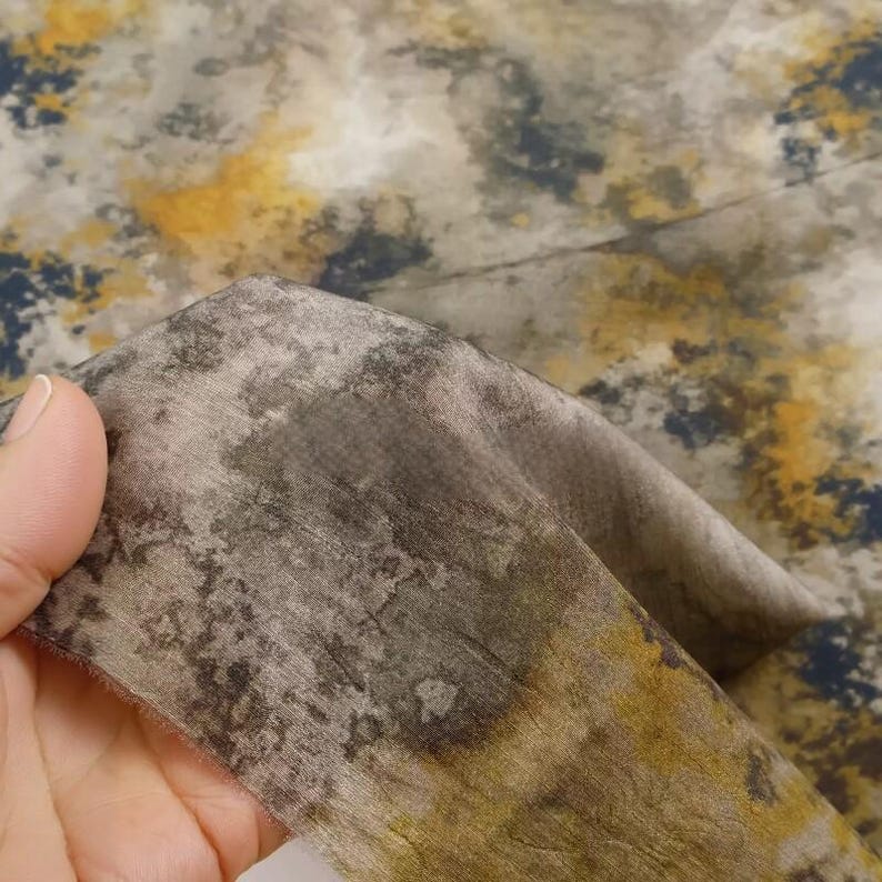 Peut inclure: Un morceau de tissu pr&eacute;sentant un motif abstrait et tachet&eacute; dans des tons de gris fonc&eacute;, charbon et jaune moutarde sourd. Le textile a un aspect textur&eacute; et l&eacute;g&egrave;rement vieilli avec des transitions de couleurs fondues sur la surface.