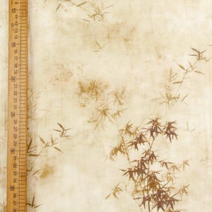 May include: A beige fabric with a bamboo leaf pattern in shades of brown. A wooden ruler with centimeter markings is visible along the left side of the fabric. The fabric has a vintage, textured appearance.