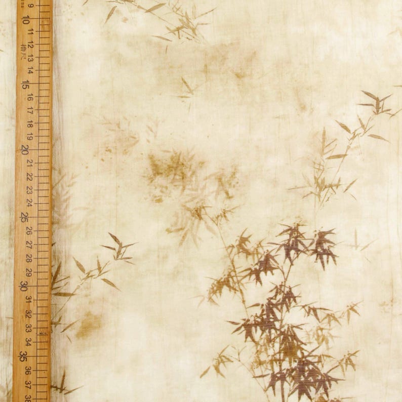 May include: A beige fabric with a bamboo leaf pattern in shades of brown. A wooden ruler with centimeter markings is visible along the left side of the fabric. The fabric has a vintage, textured appearance.