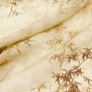 May include: Close-up of a beige fabric with a bamboo leaf pattern in shades of brown. The fabric is folded, showing the texture and design. The overall aesthetic is natural and organic.