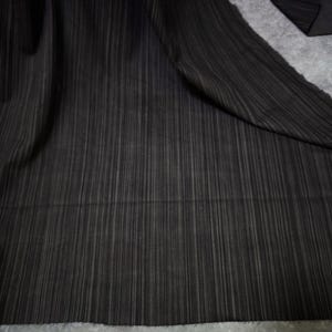 May include: A piece of black fabric featuring a subtle vertical pinstripe pattern. The material displays a consistent texture with fine, light-colored lines running parallel across the dark surface, creating a simple and uniform visual appearance.