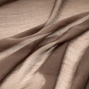 K&ouml;nnte beinhalten: Ein transparenter, leichter Stoff in einem einfarbigen Mokkabraun. Das Material weist ein feines, halbtransparentes Gewebe mit einer subtilen horizontalen Textur auf und ist in weichen, flie&szlig;enden Falten drapiert, die helle und dunkle Braunt&ouml;ne erzeugen.