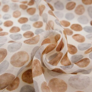 May include: Off-white fabric with a repeating pattern of brown and gray oval shapes. The fabric is draped, showing the texture and pattern variation. The design is reminiscent of pebbles or organic forms.