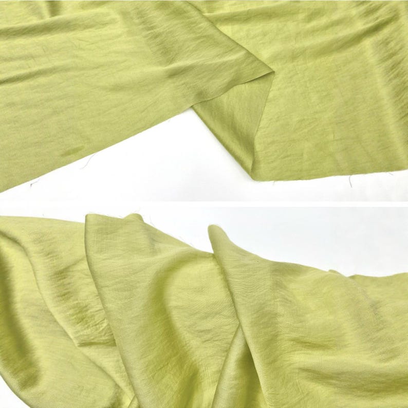 May include: A length of light lime green fabric with a subtle, fine-grained texture. The material is shown in two sections, displaying soft, flowing folds and a matte finish that catches the light across its surface, highlighting the weave.
