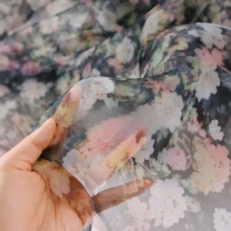 Pu&ograve; includere: Tessuto trasparente con motivo floreale nei toni del rosa, bianco, giallo e verde su sfondo scuro. Il tessuto &egrave; sollevato, mostrando la sua qualit&agrave; traslucida. Il design floreale &egrave; dettagliato e sembra uno stile acquerello.