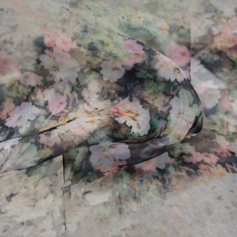 Pu&ograve; includere: Un tessuto trasparente con motivo floreale. Il design presenta un mix di fiori rosa, bianchi e verdi su uno sfondo tenue. Il tessuto &egrave; drappeggiato, mostrando la sua consistenza e il modo in cui cattura la luce.