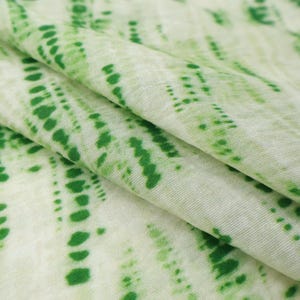 Op de afbeelding: Een stuk stof met een lichtcr&egrave;me basiskleur en een herhalend patroon van verticale, gestippelde lijnen in verschillende tinten groen. Het textiel heeft een zachte, licht getextureerde uitstraling met zichtbare plooien die diepte cre&euml;ren.