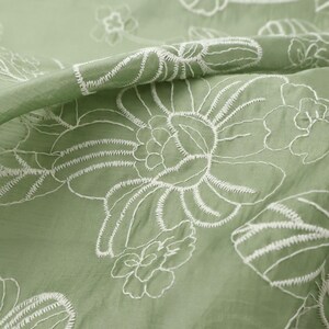 May include: A sage green fabric featuring a delicate white embroidered floral pattern. The embroidery consists of thin, continuous lines forming large, stylized blossoms and leaves across the surface of the lightweight, slightly translucent textile.