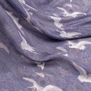 May include: Close-up of a fabric with a repeating pattern of white cranes and cloud motifs on a muted purple background. The fabric is draped, showing folds and texture. The design evokes a sense of elegance and tranquility.