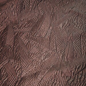 May include: A dark brown fabric featuring a repeating embossed pattern of overlapping fern leaves. The material has a textured, slightly metallic sheen with deep ridges that define the veins and edges of each individual leaf shape throughout.