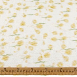 May include: A white fabric with a crinkled texture featuring a repeating pattern of soft yellow floral shapes and light green stems. A wooden ruler is positioned at the bottom, showing measurements from 19 to 45 inches across the fabric width.