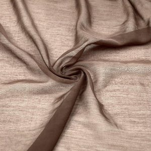 K&ouml;nnte beinhalten: Ein transparenter, leichter Stoff in einem ged&auml;mpften Taupe- oder Hellbraunton. Das Material weist eine feine, horizontale Webstruktur auf und ist in weichen, flie&szlig;enden Falten drapiert, die seine Transparenz und Zartheit unterstreichen.