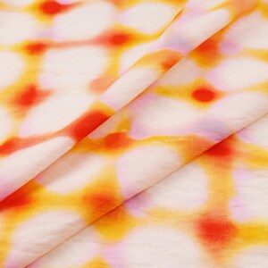 May include: Close-up of a folded fabric with a tie-dye pattern. The fabric features a white base with a repeating pattern of orange, yellow, and red circular shapes. The fabric is soft and appears to be lightweight.