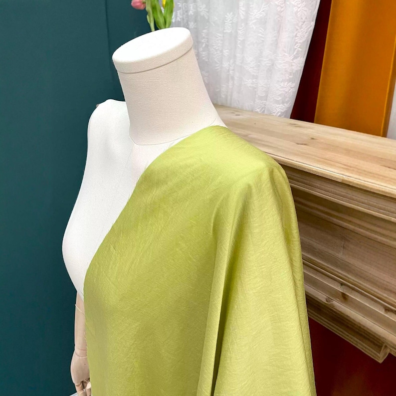 May include: A light green fabric draped over a beige mannequin torso. The textile features a visible woven texture with a matte finish, showing a consistent lime green hue across the surface as it hangs from the shoulder area of the form.