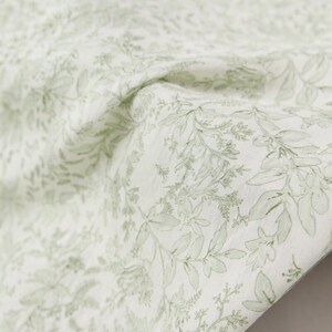Puede incluir: Tela blanca con un delicado patr&oacute;n de hojas y tallos verdes. La tela est&aacute; drapeada, mostrando la textura y el dise&ntilde;o bot&aacute;nico repetido. Las hojas var&iacute;an en tama&ntilde;o y forma, creando una sensaci&oacute;n natural y org&aacute;nica.