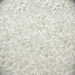 Puede incluir: Primer plano de una tela con un patr&oacute;n floral repetido. El dise&ntilde;o presenta hojas y flores de color verde claro sobre un fondo blanco. El patr&oacute;n es detallado y cubre toda la superficie.