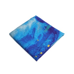 May include: Square blue and white patterned fabric with yellow accents. The fabric has a watercolor-like design with shades of blue and white. The fabric is folded into a square shape.