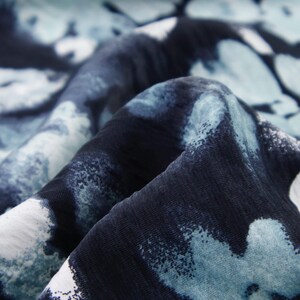 May include: Close-up of a fabric with a blue and white abstract pattern. The fabric appears to be folded, revealing the texture and design. The pattern features irregular shapes and a mix of light and dark blue hues.