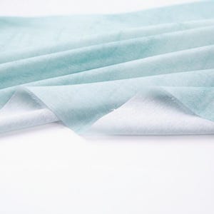 K&ouml;nnte beinhalten: Nahaufnahme eines hellblauen Stoffes mit Aquarelleffekt. Der Stoff ist gefaltet und drapiert und zeigt eine weiche Textur und einen Farbverlauf von Wei&szlig; zu Hellblau. Der Stoff wirkt leicht und luftig.