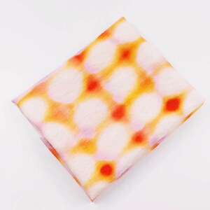May include: A folded square scarf with a repeating pattern of white, orange, and red shapes. The scarf has a soft, translucent appearance. The design features a grid-like arrangement of the colorful shapes.