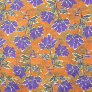 May include: An orange fabric with a repeating floral pattern. The flowers are purple with white accents, and the stems and leaves are green. The background has a textured appearance.