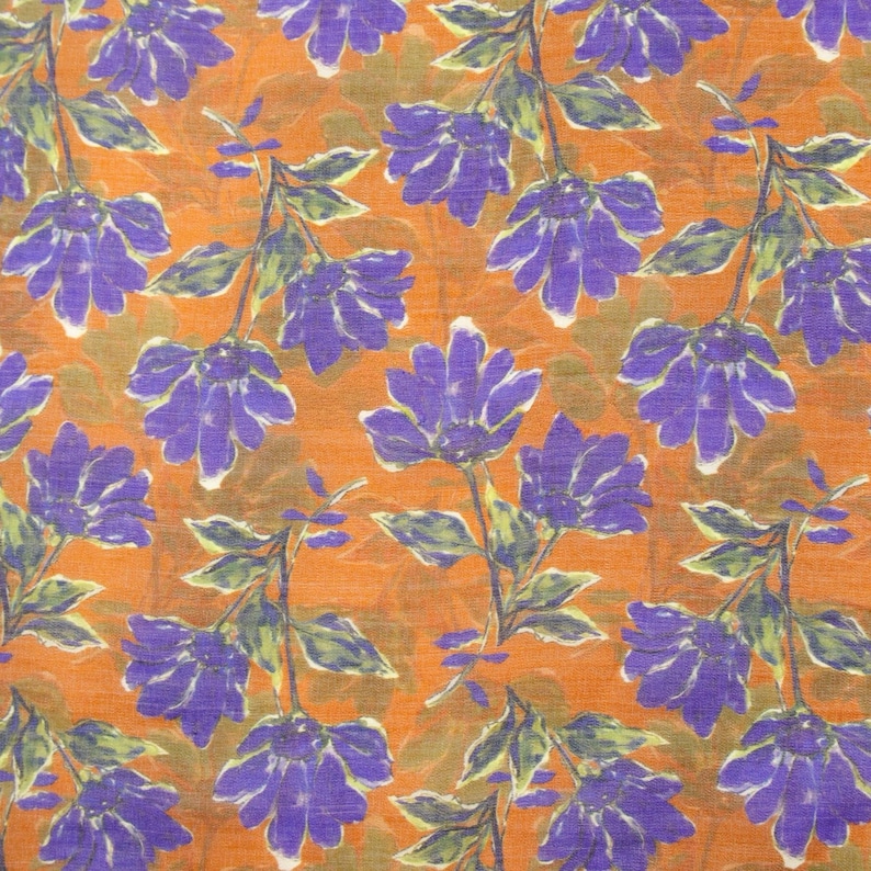 May include: An orange fabric with a repeating floral pattern. The flowers are purple with white accents, and the stems and leaves are green. The background has a textured appearance.