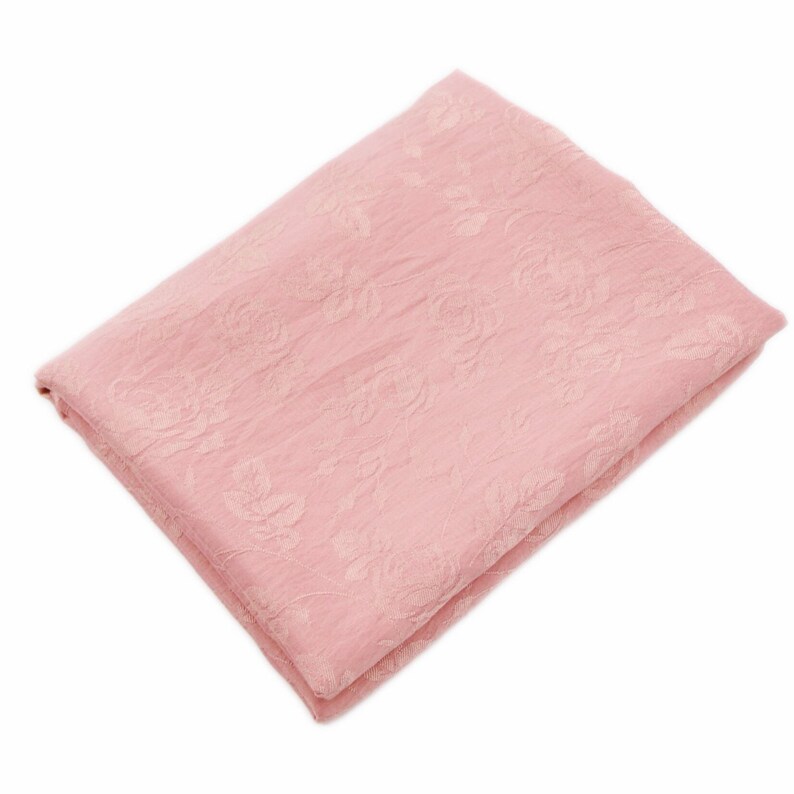 May include: A folded piece of light pink fabric featuring a subtle, tone-on-tone floral pattern with visible rose motifs. The material has a slightly crinkled, textured surface and is arranged in a neat, rectangular stack against a white background.