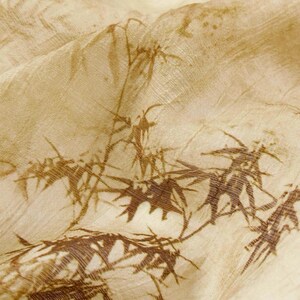 May include: Close-up of a beige fabric with a brown bamboo leaf pattern. The fabric has a slightly wrinkled texture, with the bamboo design appearing in varying shades of brown, creating a natural and organic aesthetic.