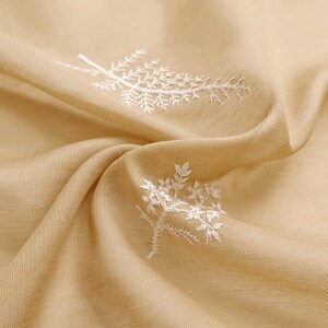 May include: Close-up of a beige fabric with white embroidered floral designs. The fabric is draped, showing folds and texture. The embroidery features delicate, detailed botanical patterns, adding a touch of elegance to the textile.