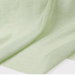 May include: A close-up of a light green fabric with a subtle floral pattern. The fabric is draped, showing folds and textures. The color is a soft, pastel green, and the material appears to be lightweight and flowing.