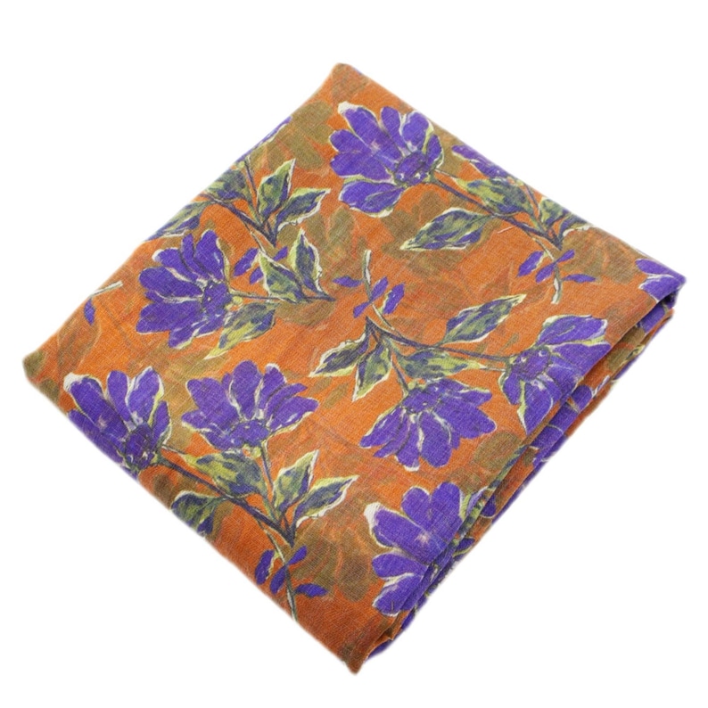 May include: Folded orange fabric with a floral pattern. The design features large purple flowers with green leaves and stems. The fabric is folded neatly, showcasing the repeating pattern. The overall aesthetic is bright and colorful.
