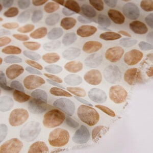 May include: Close-up of a fabric with a repeating pattern of brown and gray oval shapes on a white background. The fabric has a soft, textured appearance, with a frayed edge visible on the right side.