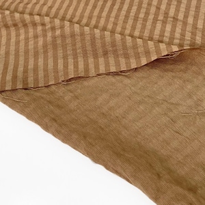 Peut inclure: Un morceau de tissu pr&eacute;sentant un motif &agrave; rayures marron clair et marron fonc&eacute; sur la partie sup&eacute;rieure, passant &agrave; un tissu textur&eacute; marron clair uni sur la partie inf&eacute;rieure. Le mat&eacute;riau a un tissage visible et des bords effiloch&eacute;s le long de la couture.