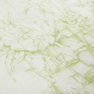 May include: Close-up of a white fabric with a delicate, repeating floral pattern in a soft, muted green. The design appears to be sketched or drawn, creating a textured and artistic effect. The fabric is slightly wrinkled, adding depth.