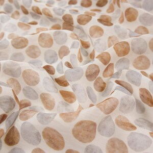 May include: Close-up of a fabric with a pattern of irregular, rounded shapes in shades of brown and gray against a cream background. The fabric is soft and flowing, with visible folds and creases, suggesting a lightweight material.