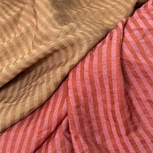 Peut inclure: Un tissu textile pr&eacute;sentant deux sections distinctes de mat&eacute;riau ray&eacute;. Une section affiche un motif &agrave; rayures en chevron brun clair et beige, tandis que l'autre section pr&eacute;sente des rayures verticales dans des tons altern&eacute;s de rose et de rouge fonc&eacute;.