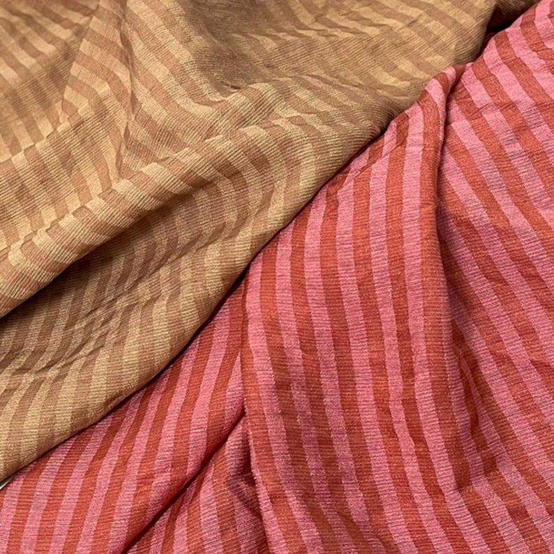 Peut inclure: Un tissu textile pr&eacute;sentant deux sections distinctes de mat&eacute;riau ray&eacute;. Une section affiche un motif &agrave; rayures en chevron brun clair et beige, tandis que l'autre section pr&eacute;sente des rayures verticales dans des tons altern&eacute;s de rose et de rouge fonc&eacute;.