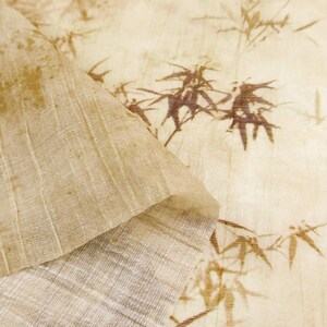May include: Close-up of a textured, beige fabric with a bamboo leaf pattern in brown. The fabric is folded over, revealing a lighter, ribbed underside. The overall aesthetic is natural and organic, suitable for home decor or craft projects.