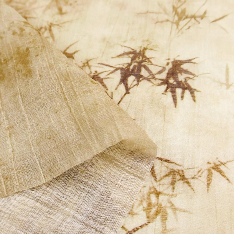 May include: Close-up of a textured, beige fabric with a bamboo leaf pattern in brown. The fabric is folded over, revealing a lighter, ribbed underside. The overall aesthetic is natural and organic, suitable for home decor or craft projects.