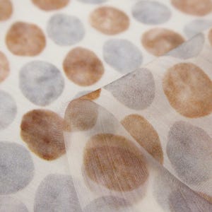 May include: Off-white fabric with a repeating pattern of large, watercolor-style ovals in shades of brown and gray. The fabric is slightly translucent, with a soft, flowing drape. The design is reminiscent of pebbles or organic shapes.