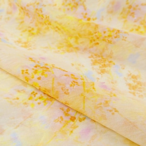 May include: A close-up of a fabric with a floral pattern. The fabric is a light yellow color with a pattern of yellow and orange flowers and green stems. The fabric is folded over, showing the texture and detail of the design.