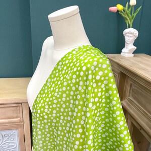 May include: A vibrant lime green fabric featuring a pattern of white polka dots of varying sizes. The textile is draped over a white mannequin torso, showcasing the lightweight texture and the consistent distribution of the circular white print.