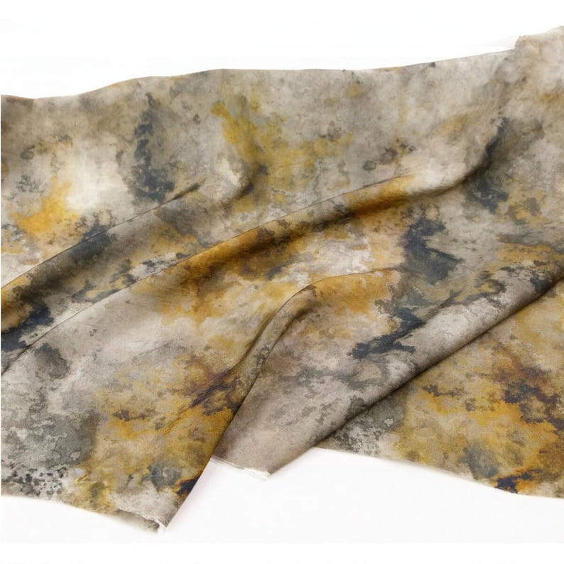 Peut inclure: Un morceau de tissu pr&eacute;sentant un motif abstrait et tachet&eacute; dans des tons de jaune moutarde, gris anthracite et blanc cass&eacute;. Le textile affiche une texture douce et pliss&eacute;e avec des taches de couleur irr&eacute;guli&egrave;res cr&eacute;ant un aspect nuageux.