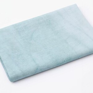 K&ouml;nnte beinhalten: Ein gefalteter, hellblauer Stoff mit subtilen Farbvariationen. Das Material wirkt weich und m&ouml;glicherweise strukturiert, mit leichtem Glanz. Die Gesamtfarbe ist ein ged&auml;mpftes, pastellblau, geeignet f&uuml;r verschiedene Bastel- oder Textilprojekte.