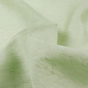 May include: Close-up of a light green fabric with a subtle textured pattern. The fabric appears to be soft and flowing, with gentle folds and highlights. The overall impression is of a delicate, high-quality textile.