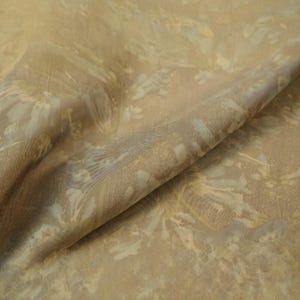 May include: Close-up of a fabric with a floral pattern. The fabric has a beige background with a subtle texture. The floral design features light beige and pale blue accents, creating a soft, natural look. The fabric is folded, showing its drape.